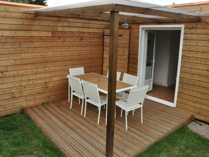 Exterior view of the PMR cottage with wooden deck and garden furniture, available for rent at the 3-star Le Paquier Fané campground in Saône-et-Loire.