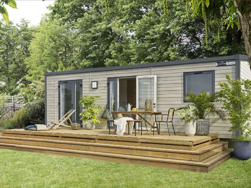 Exterior view of the 2-4 person mobile home with 9 m² wooden terrace and garden furniture, available to rent at the 3-star Le Paquier Fané campsite in Saône-et-Loire.